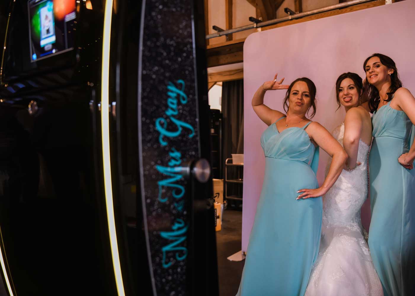 Bride and bridesmaids posing beside a personalised Fusion Mirror Booth at a wedding