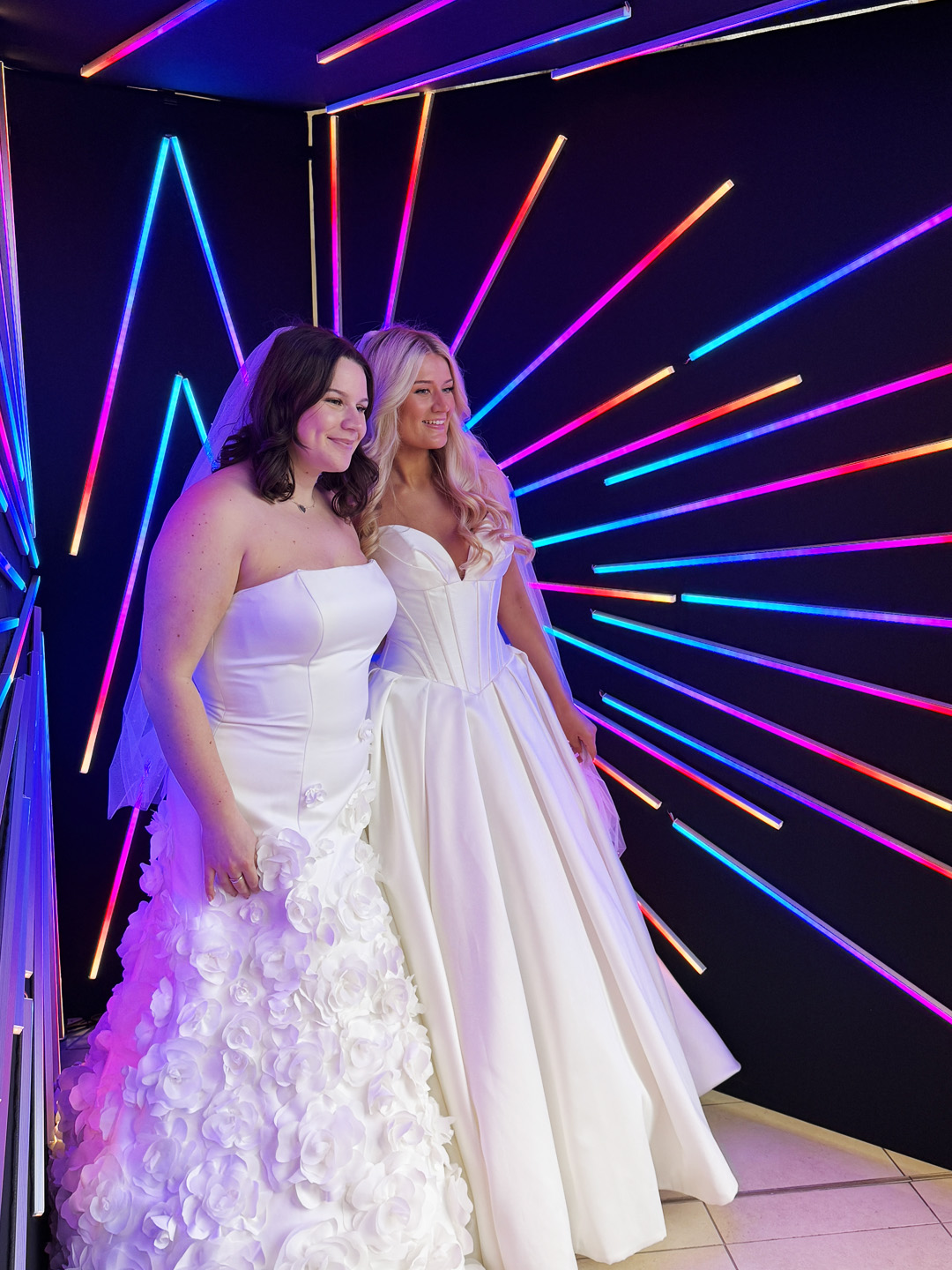 Two brides posing together in the illuminated Vogue Booth at their wedding