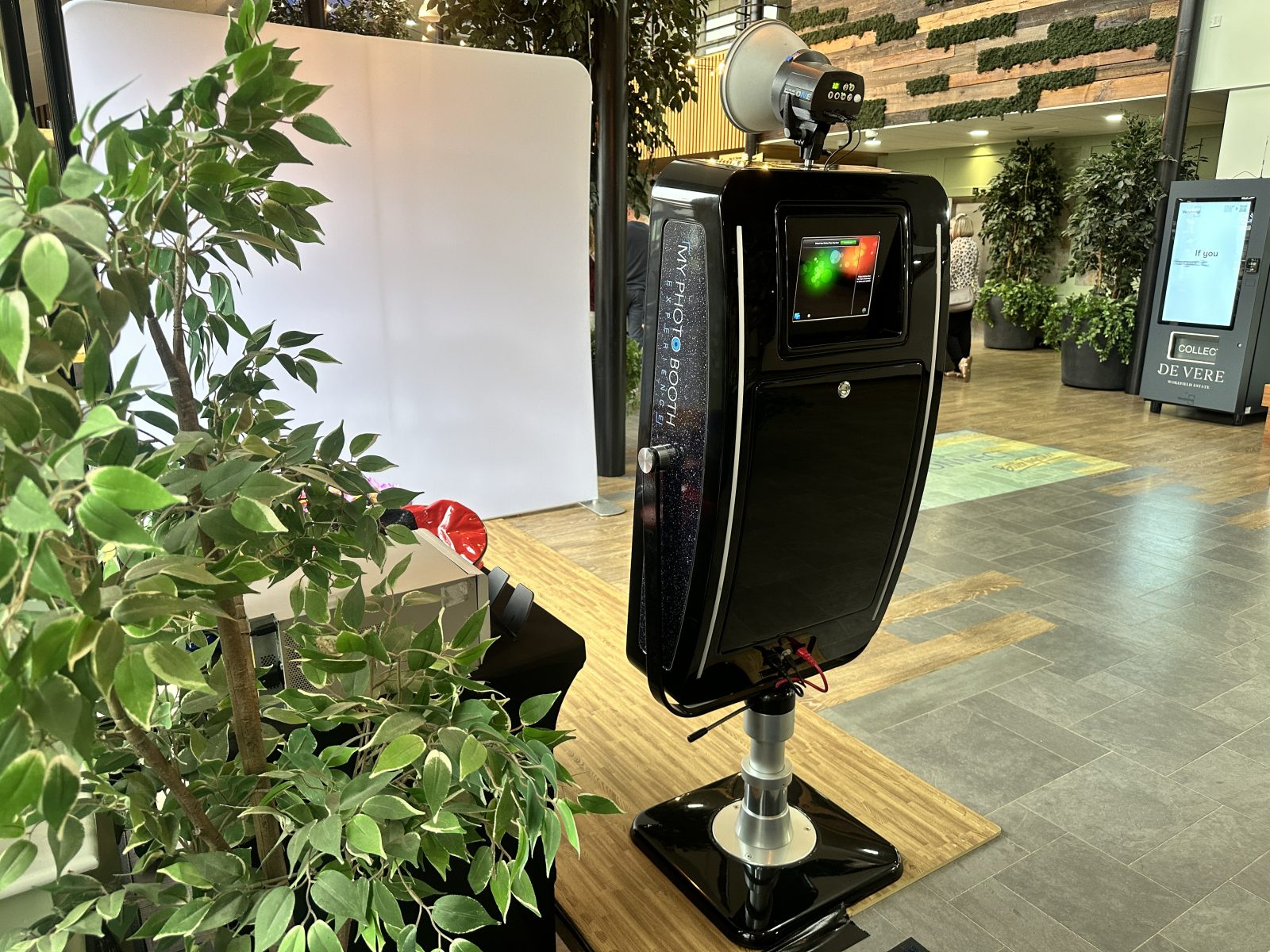 Classic enclosed photo booth with a glowing screen beside indoor plants