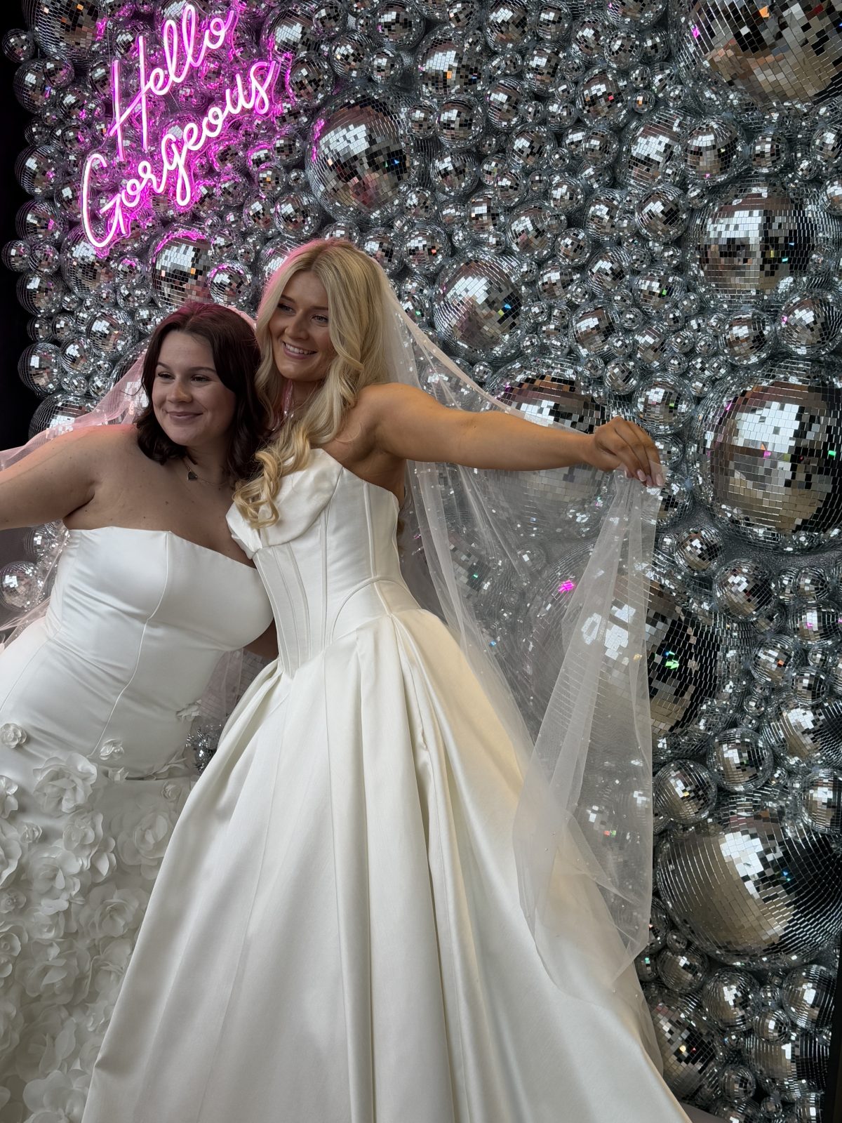 Two brides posing together in front of a sparkling Disco Wall