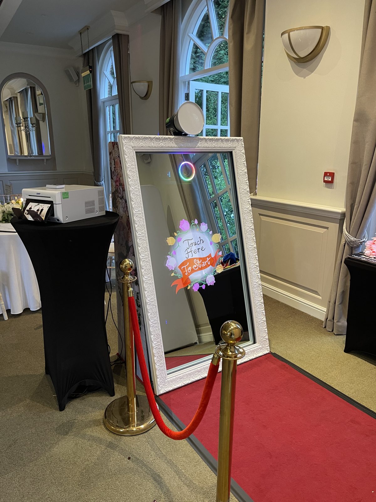 White framed Magic Mirror photo booth with props beside a window